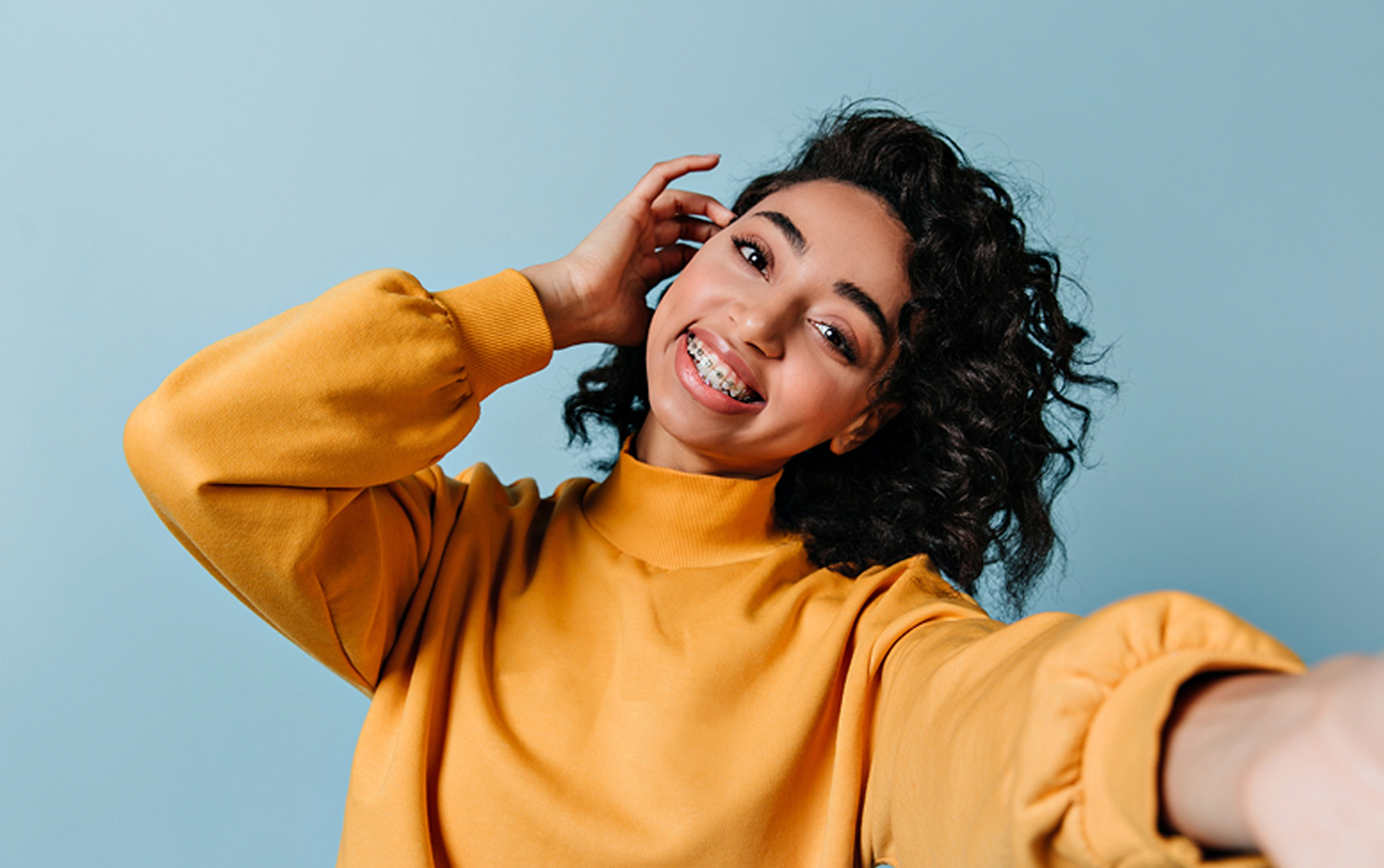 Happy Dark Haired Woman With Braces Pulling Her Hair Aside