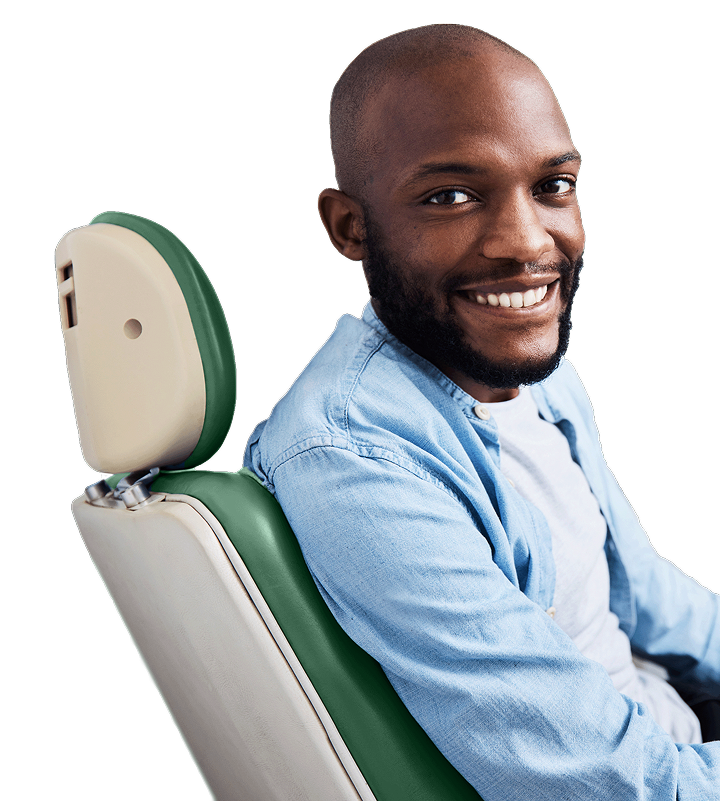 A happy dark skinned man smiling in an examining chair, wearing a blue shirt.