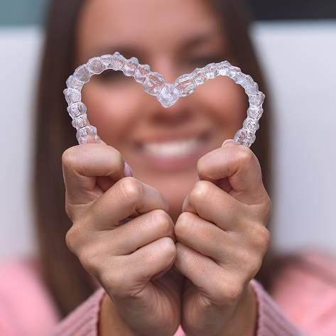 Woman Holding Pair Of Clear Aligners In Heart Shape