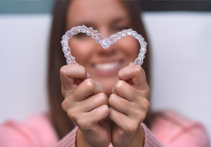 Woman Holding Pair Of Clear Aligners In Heart Shape