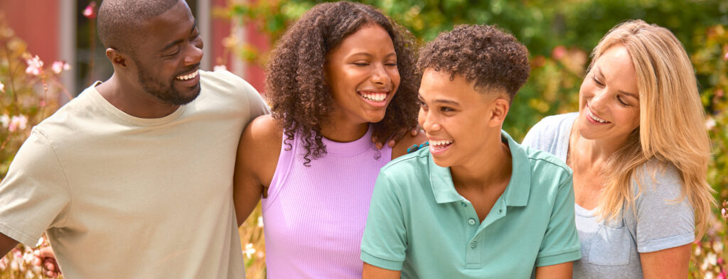 Portrait Of Two Teenage Children Standing With Parents Outdoors At Home In Summer Garden
