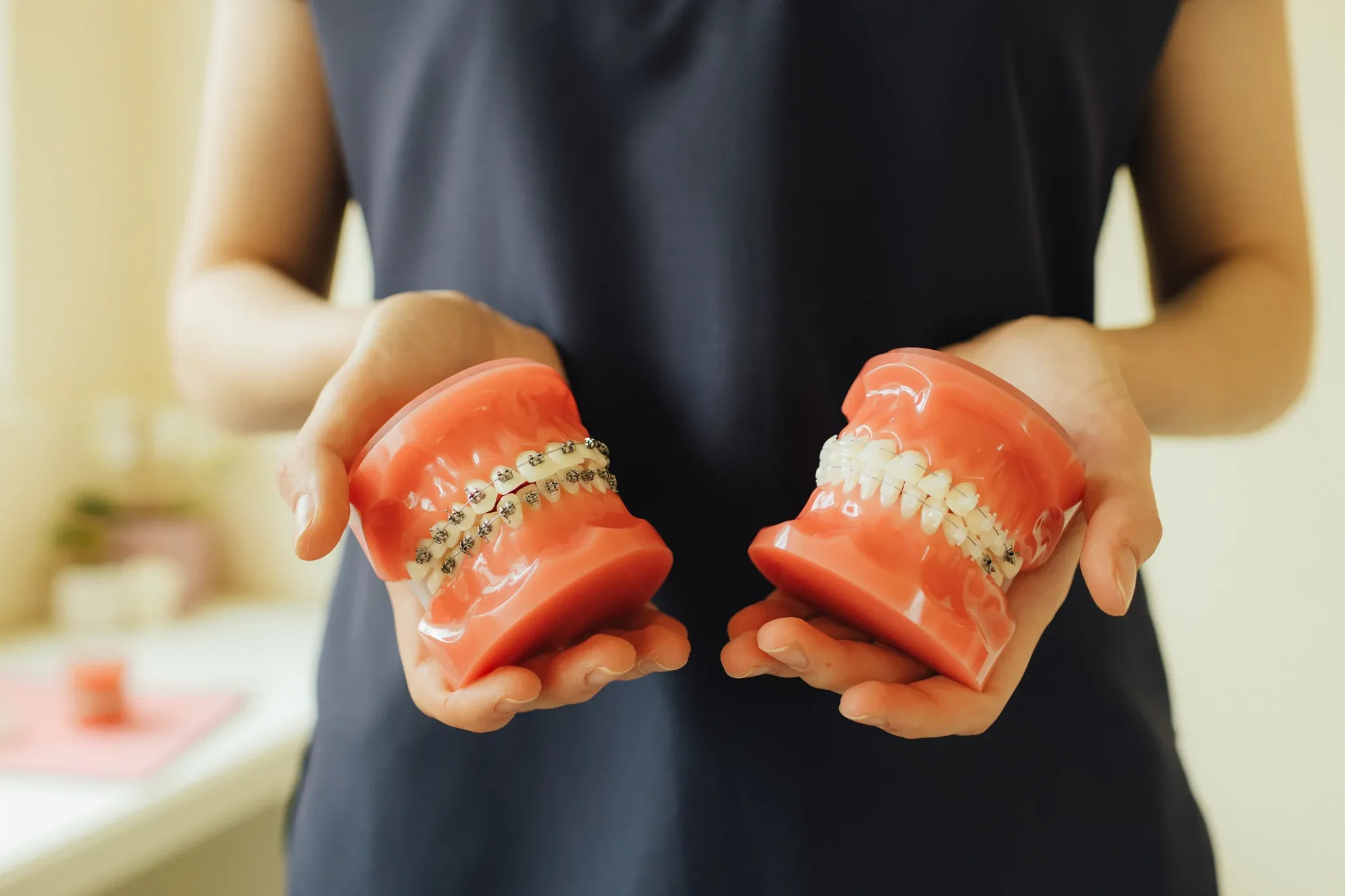 Close Up Of An Orthodontist Hands Showing Two Artificial Jaws One With Clear Braces And The Other With Metal Braces Copy